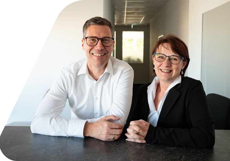 Junge, grinsende Person mit Seitenscheitel, langem, goldblondem Haar, Brille und khakifarbener Bluse.